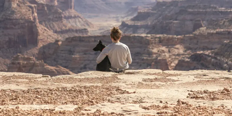 Frau sitzt mit ihrem Hund am Rand einer Schlucht und blickt in die Landschaft