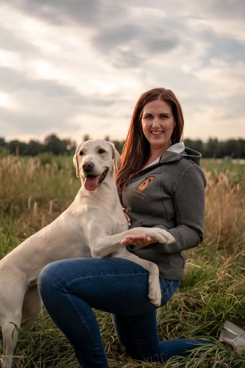 Christina Hofer kniet neben ihrer Labradorhündin Betty auf einer Wiese